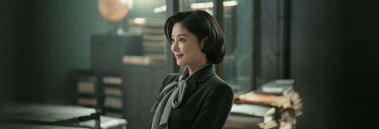 Kim Yoo-jung como Lee Ga-gyeong, com roupa verde escura em uma sala de documentos