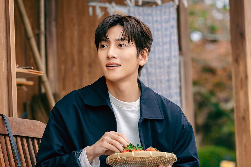 Ji Chang-wook como Yu-bin, de jaqueta escura, sentado com uma cesta de morangos na mão
