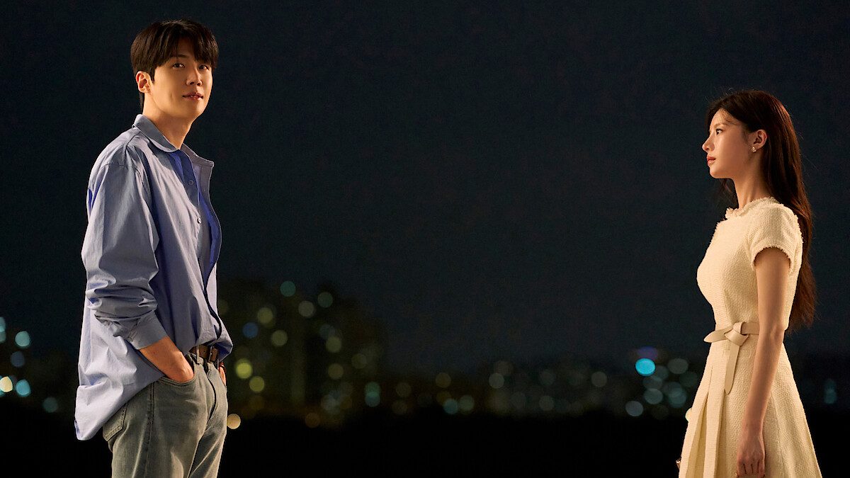 Kim Seon-ho e Go Youn-jung, como Ho-jin e Mu-hee, de pé frente a frente à noite com luzes da cidade ao fundo