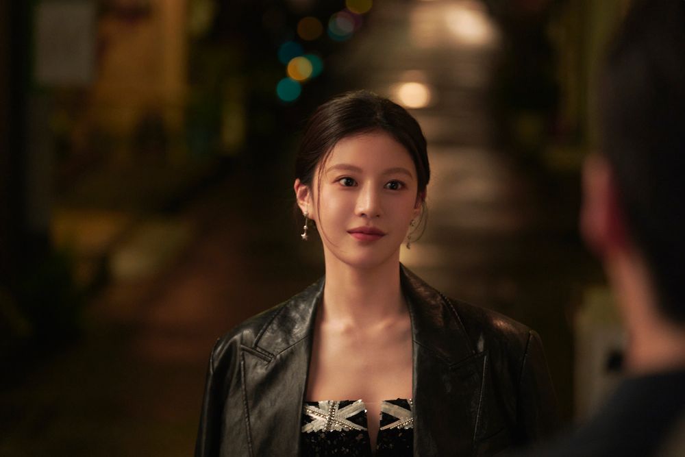 Go Youn-jung como Mu-hee, de jaqueta de couro preta, sorri numa rua à noite