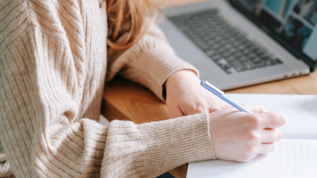 Mãos fazem anotações em um caderno ao lado de um computador