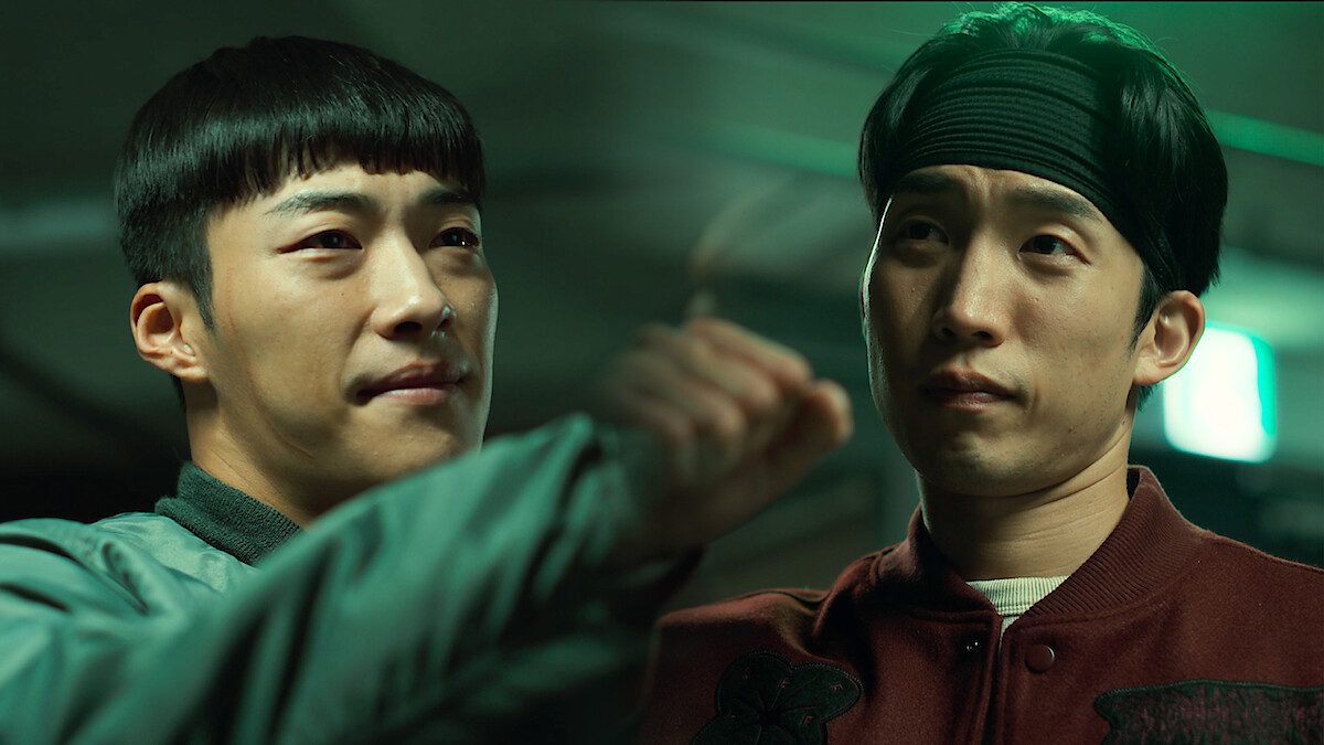 Woo Do-hwan e Lee Sang-yi lado a lado sob luz verde, um deles com o punho erguido