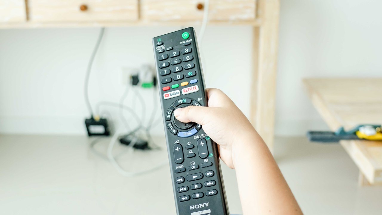 Mão segura controle remoto diante da televisão