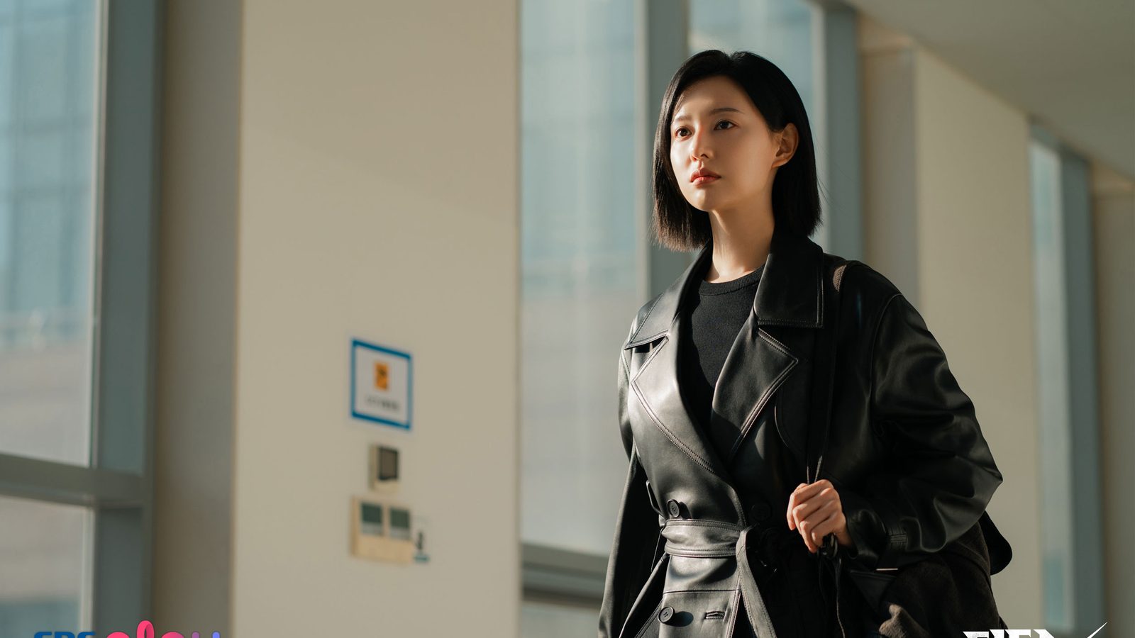 Kim Ji-won como Gye Su-jeong, de casaco longo de couro preto, caminha por um corredor claro de hospital