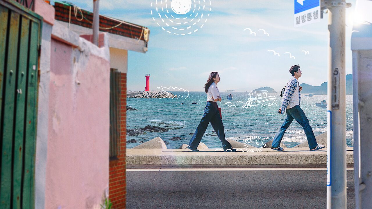 Hye-jin e Du-sik caminhando diante do mar em imagem oficial de Hometown Cha-Cha-Cha