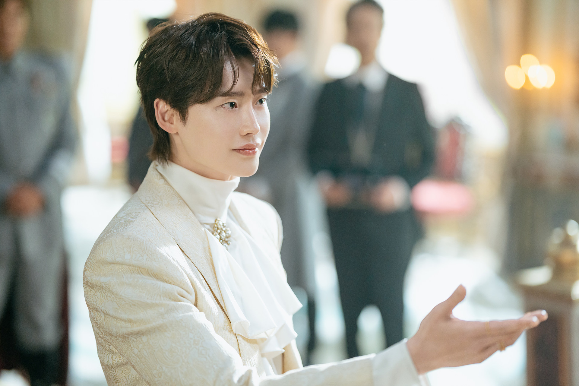 Lee Jong-suk como Heinrey, em traje claro e com uma mão estendida