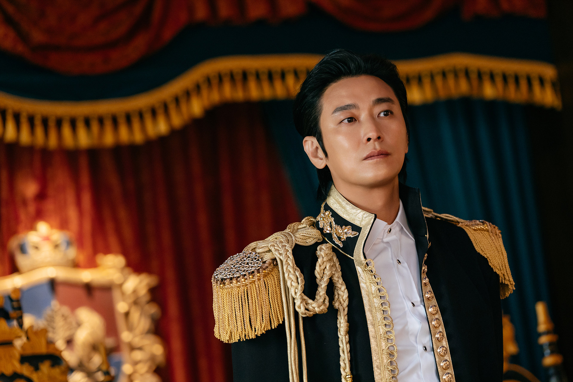 Ju Ji-hoon como Sovieshu, de traje preto com detalhes dourados diante de cortinas