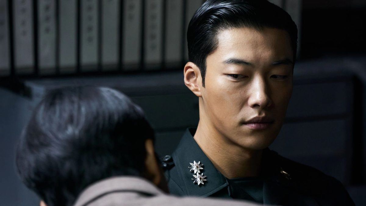 Woo Do-hwan de quepe e farda militar verde-oliva em cerimônia com oficiais ao fundo