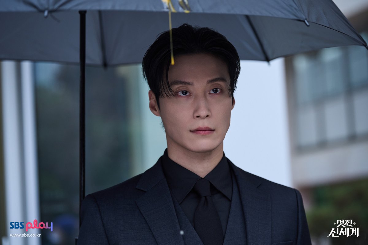 Heo Nam-jun como Cha Se-gye, de terno preto, sob um guarda-chuva preto na rua