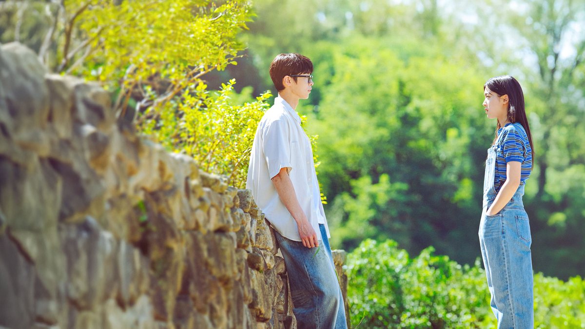 Arte de Last Summer na Viki: um rapaz de camisa branca encostado num muro de pedra olha para uma moça de jardineira jeans